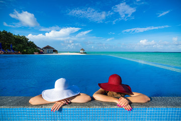 Fototapeta na wymiar Two women in a hat sitting on the edge of the swimming pool