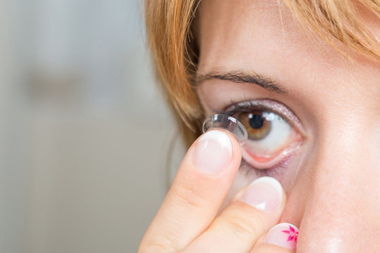 Young woman putting contact lens in her eye