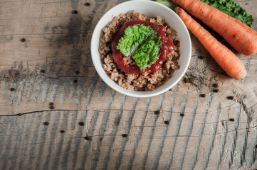 Buckwheat porridge with tomato sauce and leaf salad in a white bowl on a wooden table next to a ceramic bowl with dish is carrots or sliced carrot. Food background. Nice and tasty atmosphere.