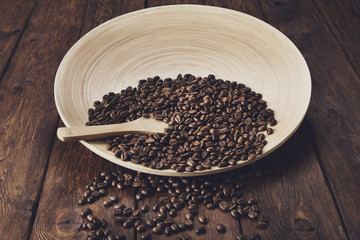 Coffee beans in bowl with wooden spoon on table