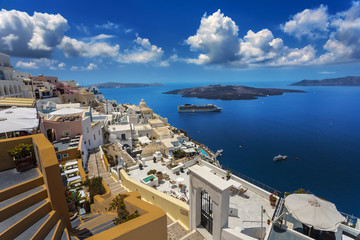 Greece. Santorini (Thira). Fira town with characteristic style for Cycladic architecture - white-washed cube houses built on the edge of high cliff. There is Nea Kameni Island in the background