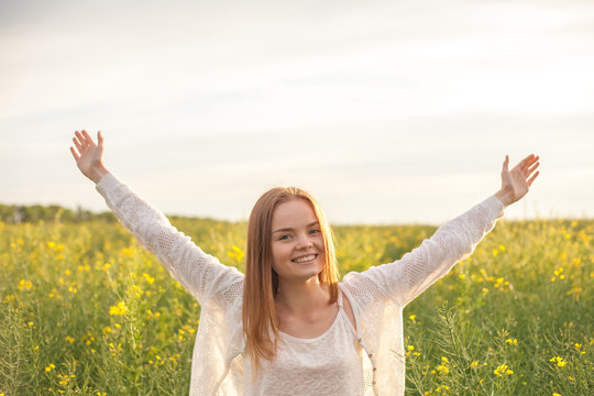 woman with open arms in the green rapeseed field at the morning.