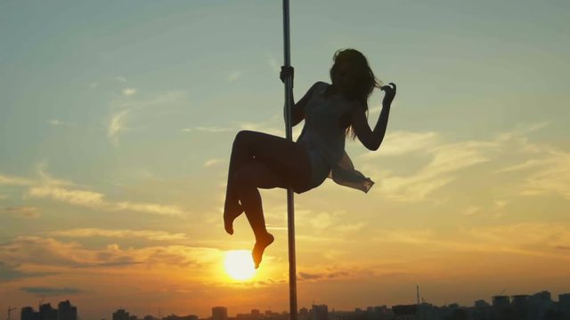 Sexy attractive girl poledancer performs advanced pole dance tricks at sunset on portable dancing stage over the skyline