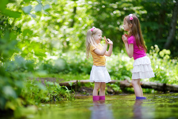 Two cute little sisters playing in a river wearing raining boots
