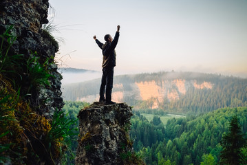 Hiker stands on top of the mountain, hands raised up