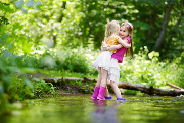 Two cute little sisters playing in a river wearing raining boots
