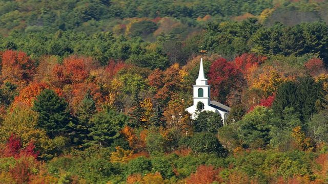 Low flight passing church amid New England autumn woods