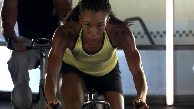 Tilt-up from wheel of stationary bicycle to woman cycling in spinning class