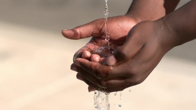 Hands of African American child capturing water in bright sunshine.
