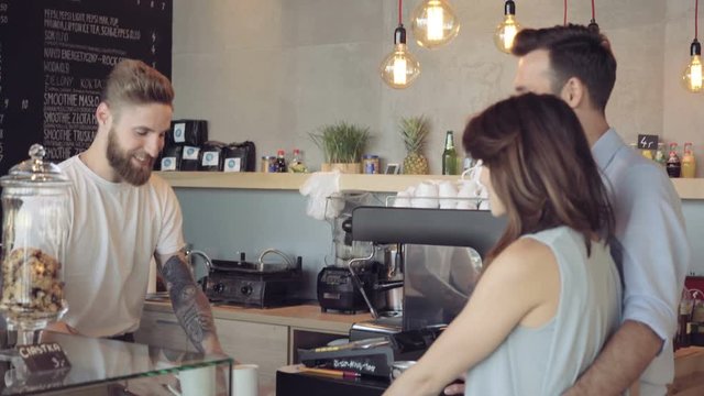 Happy barista serving coffee ordered by young couple