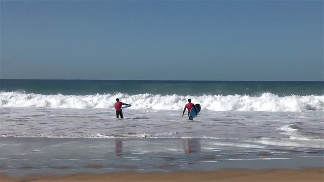 Two surf students in a beach break trying to practice their first take off on a wave.