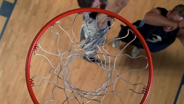 Basketball player jumping to drop ball through net, viewed in slow motion from above hoop