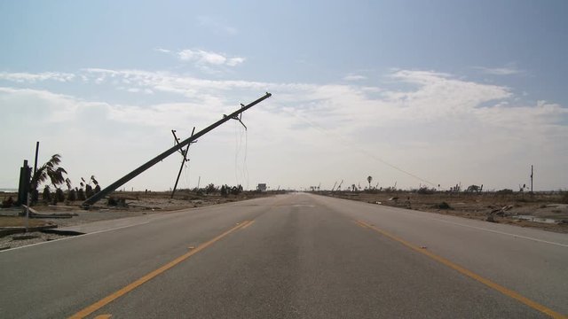 Toppled power pole with broken lines leaning over highway in aftermath of a hurricane