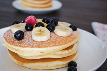 Pancakes with blueberry and bananas on white plate