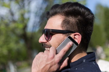 Closeup of smiling handsome bearded man in  shirt using mobile p