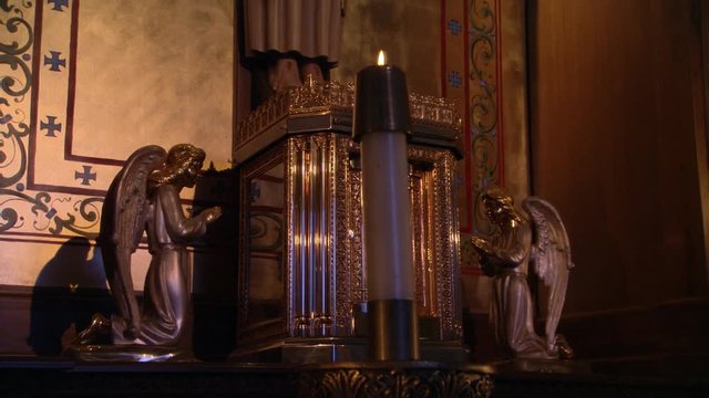 Close view of carved angels kneeling at foot of crucifix, candle through frame