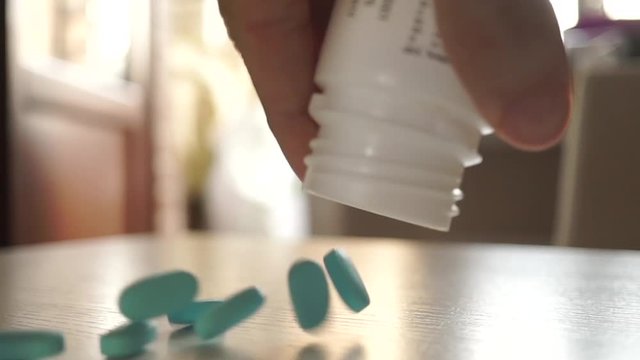 Blue pills being poured from the bottle on the table. Slow motion close up video