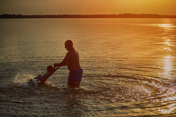 father playing with children in the water during sunset