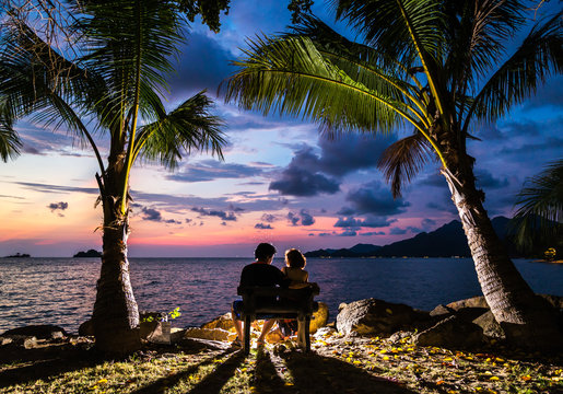 Couple silhouette cuddling and watching sun at sunset on the bea