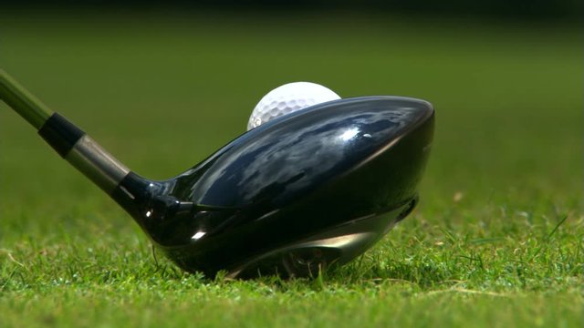 Close-up of golf club near teed ball and ball being driven from tee