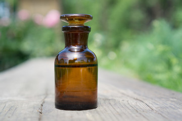 Little brown bottle with water or liquid on wooden board, against the background of vegetation.