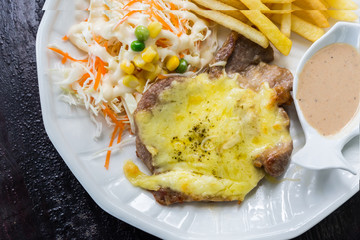 Grill pork steak under white sauce, French Fries (potato chips).