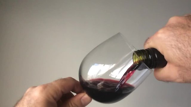 Man pouring red wine from a bottle into a wine glass over a greay background. copy space