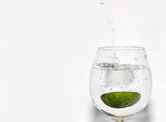 Slice of lime being dropped into a glass of drink on white background on right hand side