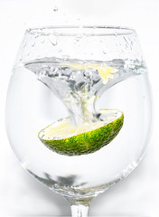 Slice of lime being dropped into a glass of drink on white background