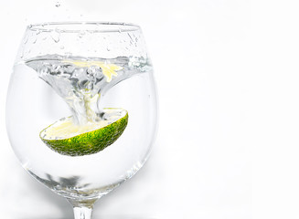 Slice of lime being dropped into a glass of drink on white background on left hand side