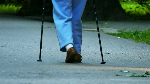 Slow motion. Old age woman with sticks for walking go in park. 