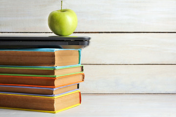 a stack of books in colorful covers near Apple on a white wooden background