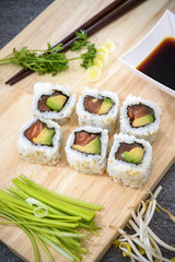 Sushi salmon rolls on cutting board with soy sauce, soy sprouts, onion grass and coriander