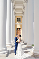 Wedding couple on the nature is hugging each other. Beautiful model girl in white dress. Man in suit. Beauty bride with groom. Female and male portrait. Woman with lace veil. Lady and guy outdoors