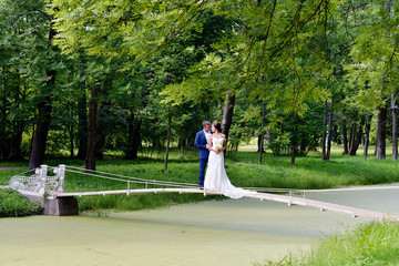 Wedding couple on the nature is hugging each other. Beautiful model girl in white dress. Man in suit. Beauty bride with groom. Female and male portrait. Woman with lace veil. Lady and guy outdoors