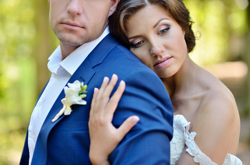 Wedding couple on the nature is hugging each other. Beautiful model girl in white dress. Man in suit. Beauty bride with groom. Female and male portrait. Woman with lace veil. Lady and guy outdoors