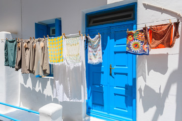 Clothes hanging in front of a house with blue door and window on whitewashed street in Mykonos town, Cyclades islands, Greece