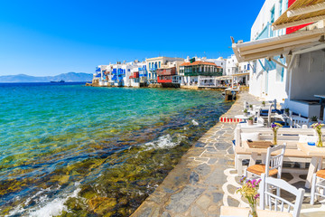Chairs with tables in typical Greek taverna in Little Venice part of Mykonos town, Mykonos island, Greece - obrazy, fototapety, plakaty