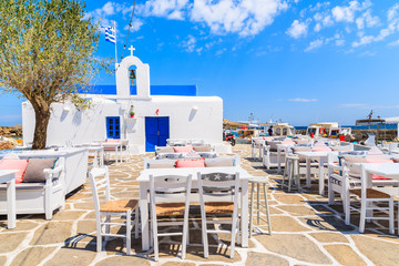 Taverna tables on a square with typical white Greek church in Naoussa port, Paros island, Cyclades, Greece