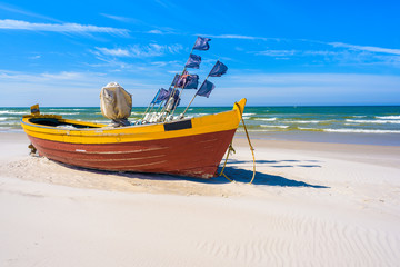 Naklejka na ściany i meble Colorful traditional fishing boat on sandy Baltic Sea beach in Debki, Poland