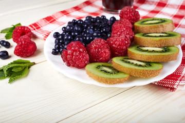 Berries on plate.Blueberry,raspberry,kiwi.Vitamin A. Vitamin C.Checkered napkin.On white wooden table.Healthy lifestyle.Diet and weight loss concept.