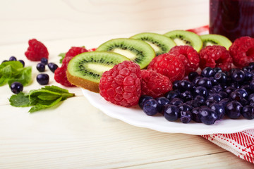 Berries on plate.Blueberry,raspberry,kiwi.Vitamin A. Vitamin C.Checkered napkin.On white wooden table.Healthy lifestyle.Diet and weight loss concept.