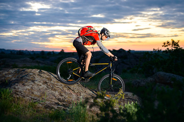 Fototapeta premium Cyclist Riding the Bike Down Hill on the Mountain Rocky Trail at Sunset