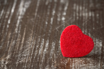 Red felt heart on wooden background.