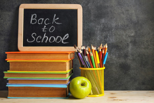 wooden plaque with the inscription "back to school" near the pencil box with school equipment and Apple with stack of books and notebooks on wooben table