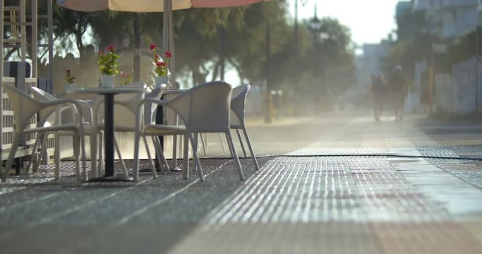 Worker washing paved sidewalk by the empty street cafe in the morning