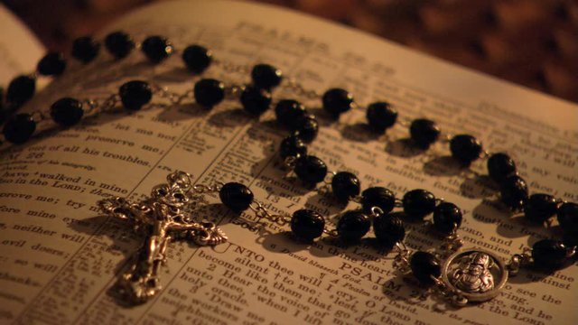 Left pan close-up of rosary lying on an open Bible