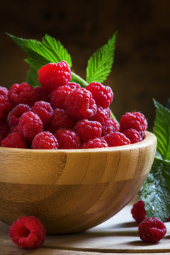 Fresh organic raspberries in bowl, green leaves, vintage wooden