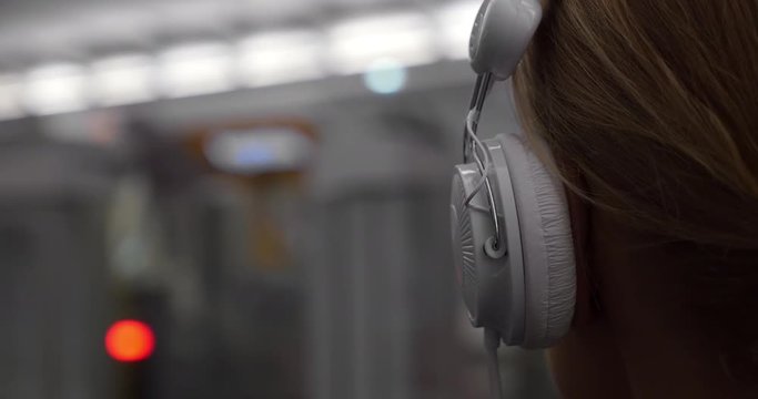 Close-up back shot of a girl in white headphones enjoying music while waiting for train in underground