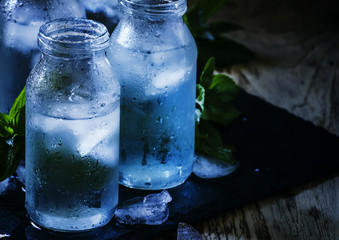 Very cold mineral water with ice in a misted glass bottles, dark